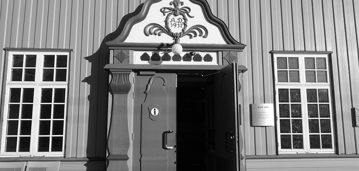The carved 1917 doorway of Oppdal station in Norway, its double door standing wide open onto the unlit hall inside, with nobody in sight